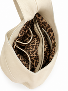 Cream leather shoulder bag shown from an overhead angle, revealing a leopard print lining with a zippered middle pocket 